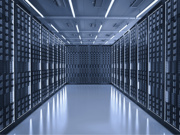 Wide-angle view of a modern data center with rows of server racks lining both sides and the back wall. The room is brightly lit with overhead fluorescent lights, and the reflective floor enhances the sleek, high-tech environment. The symmetrical layout emphasizes the scale and organization of the facility.