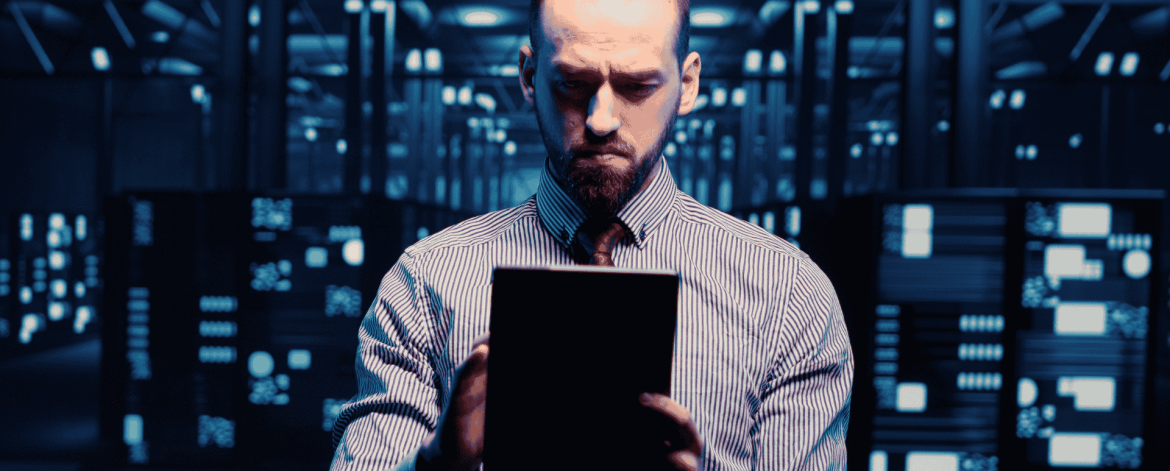 IT professional reviewing system data on a tablet inside a server room during hardware monitoring and lifecycle oversight.