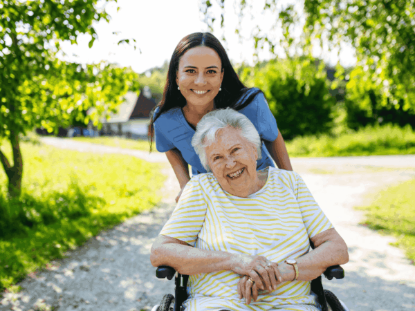 Home healthcare caregiver assisting elderly woman in wheelchair outdoors during home based care visit