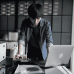 IT technician servicing mobile devices and computer hardware at a workstation, supporting hardware lifecycle management, repairs, and device replacement planning for organizations