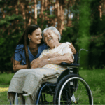 Caregiver supporting elderly woman in wheelchair outdoors highlighting the importance of reliable network infrastructure for continuous home-based care coordination.