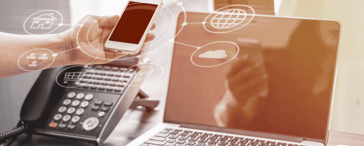 Person holding a smartphone near a laptop and office desk phone, with digital icons representing cloud computing, internet, travel, email, and shopping overlaid, symbolizing modern business communication technology.