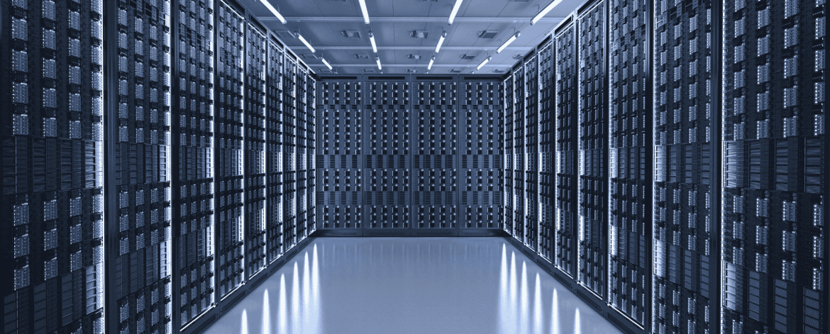 Wide-angle view of a modern data center with rows of server racks lining both sides and the back wall. The room is brightly lit with overhead fluorescent lights, and the reflective floor enhances the sleek, high-tech environment. The symmetrical layout emphasizes the scale and organization of the facility.