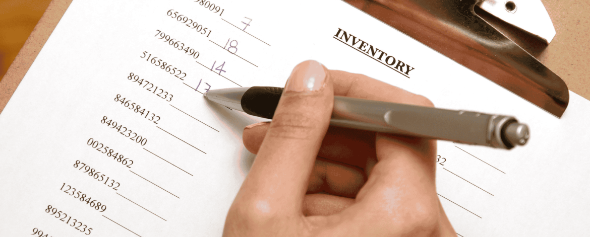 Close-up of a person writing on an inventory checklist with a pen, tracking device serial numbers on a clipboard—representing IT asset management and device inventory services provided by an MSP in the San Francisco Bay Area.