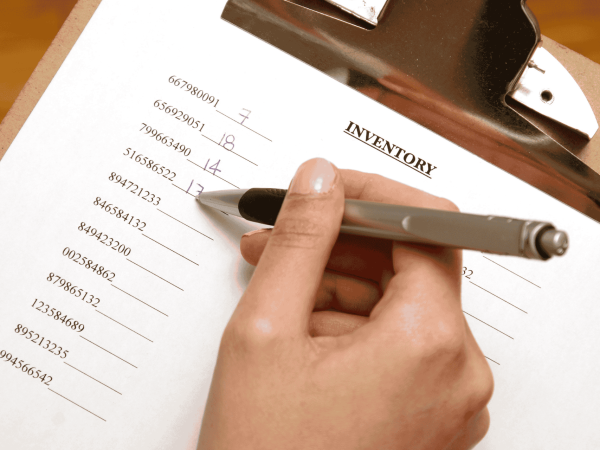 Close-up of a person writing on an inventory checklist with a pen, tracking device serial numbers on a clipboard—representing IT asset management and device inventory services provided by an MSP in the San Francisco Bay Area.
