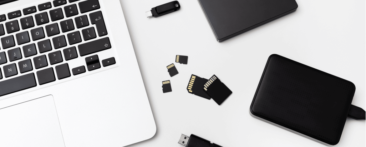 Data backup and storage solutions with laptop, external hard drives, USB flash drives, and SD cards on desk — IT Managed Services Provider in San Francisco Bay Area