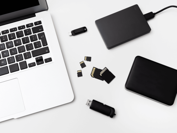 Data backup and storage solutions with laptop, external hard drives, USB flash drives, and SD cards on desk — IT Managed Services Provider in San Francisco Bay Area