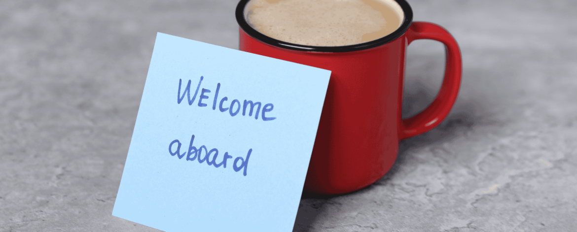 Welcome aboard note next to a coffee mug symbolizing employee onboarding – introducing new hires to company systems, technology access, and IT support.