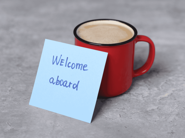 Welcome aboard note next to a coffee mug symbolizing employee onboarding – introducing new hires to company systems, technology access, and IT support.