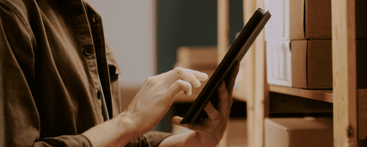 Employee using a tablet to track IT hardware inventory on storage shelves as part of lifecycle management and asset tracking.