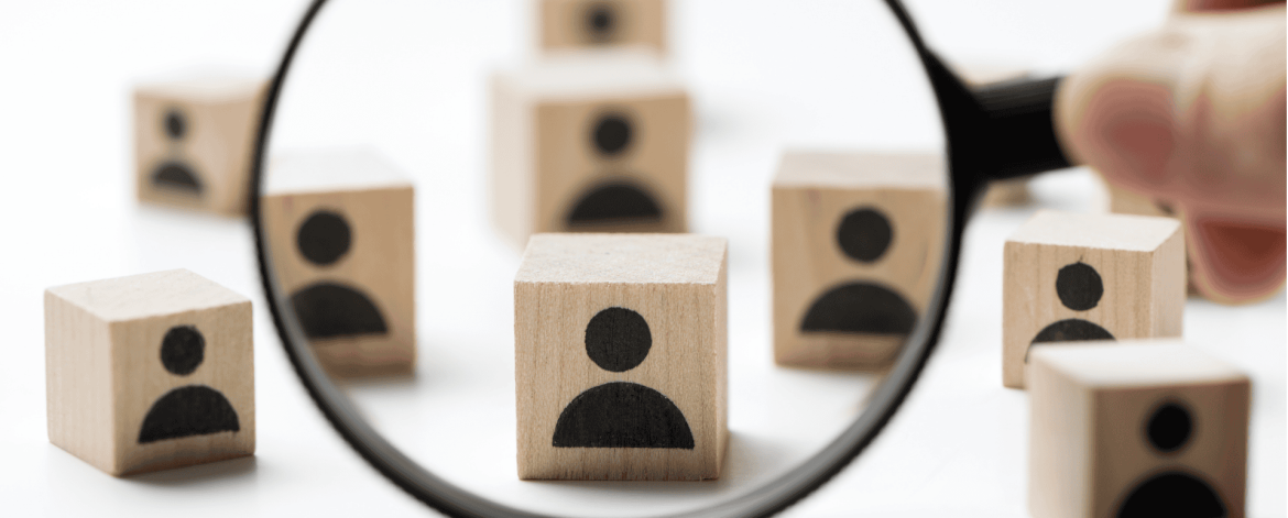 Magnifying glass focusing on a wooden block with a person icon – identifying user accounts for immediate deactivation during off-boarding.