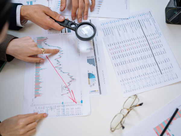 Business team analyzing financial and technology performance reports with magnifying glass to assess IT technical debt and cybersecurity risk