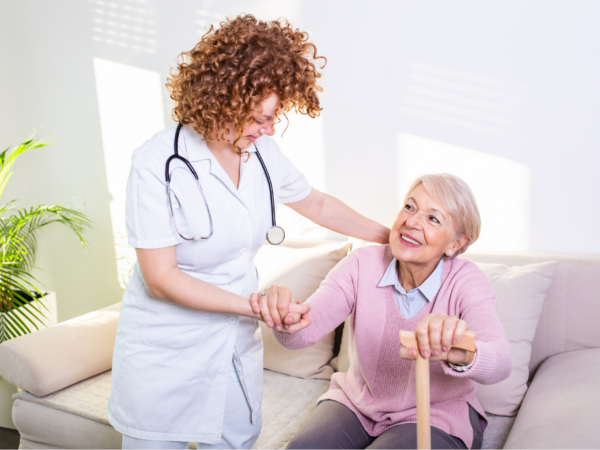 Home healthcare nurse assisting senior patient with mobility support during in home care visit supported by secure healthcare IT systems