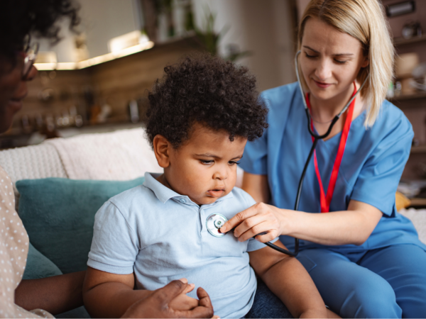 Home healthcare provider checking child patient vital signs during in home medical visit using secure healthcare technology systems.