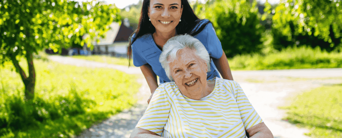 Home healthcare caregiver assisting elderly woman in wheelchair outdoors during home based care visit