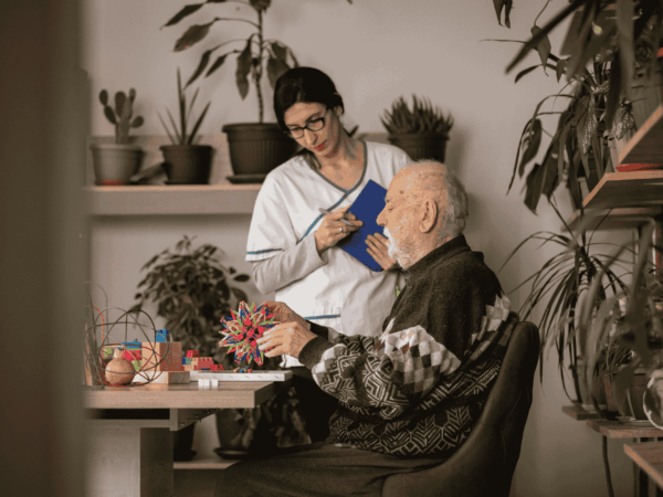 Healthcare worker monitoring elderly patient activity during home visit representing secure handling of patient data through endpoint protection solutions.