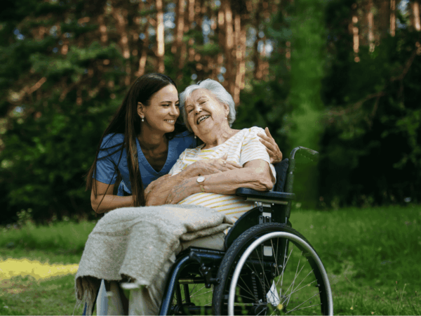 Caregiver supporting elderly woman in wheelchair outdoors highlighting the importance of reliable network infrastructure for continuous home-based care coordination.