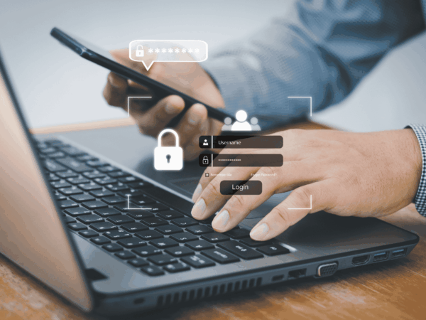 Business professional using smartphone and laptop with secure login screen representing multi factor authentication for home-based care organizations