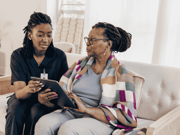 Home caregiver assisting elderly woman with conversation and daily support in a home-based care setting emphasizing trust and communication