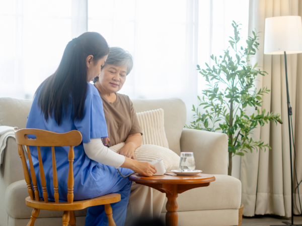In home caregiver checking senior patient vital signs during home based care visit supported by compliant healthcare technology