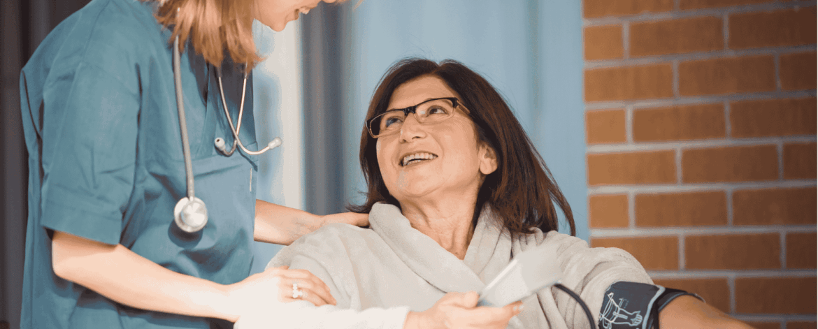 Nurse checking blood pressure of senior patient in home setting emphasizing importance of protecting connected medical devices with endpoint security.