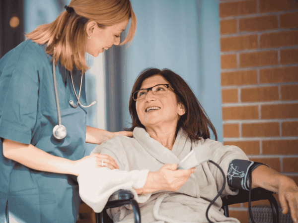 Nurse checking blood pressure of senior patient in home setting emphasizing importance of protecting connected medical devices with endpoint security.