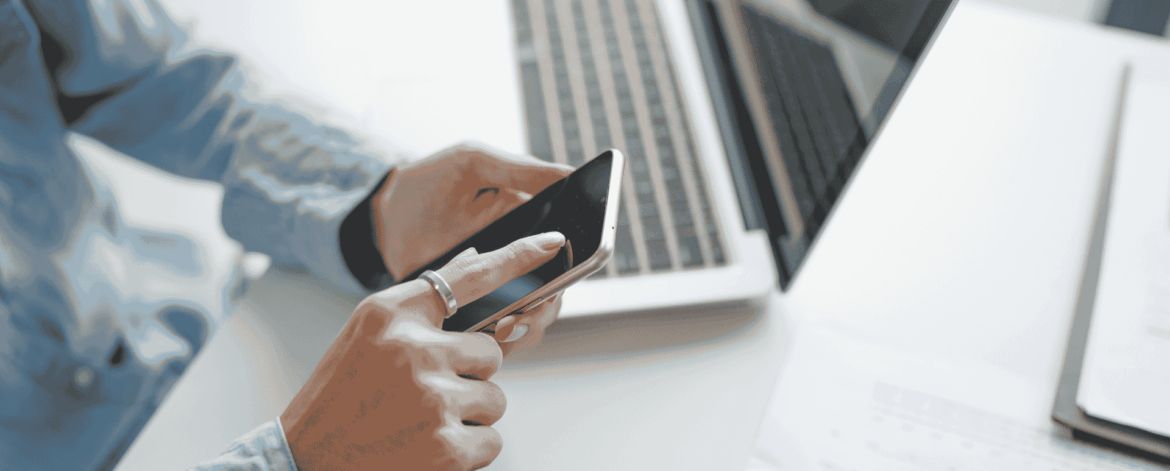 Home-based care professional using a smartphone alongside a laptop, representing mobile device security and MDM best practices for home health agencies.