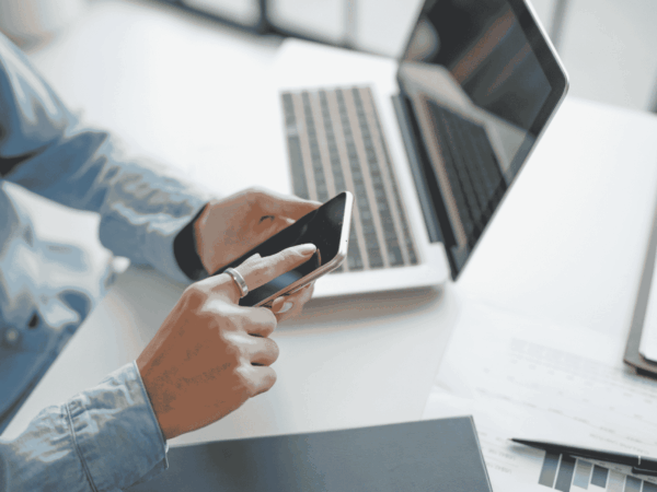 How Home Based Care Companies Can Manage and Secure their Teams Mobile Devices 3 Home-based care professional using a smartphone alongside a laptop, representing mobile device security and MDM best practices for home health agencies.