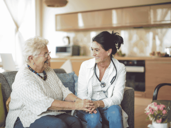 Older woman smiling and holding hands with a healthcare professional during an in-home visit.
