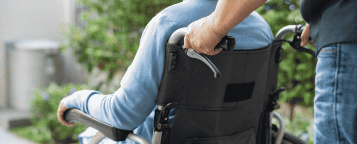 Caregiver pushing an older adult in a wheelchair along an outdoor path, the kind of field visit a HIPAA risk assessment for home health agencies has to account for.