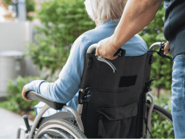 Image 1_8.24.26 Caregiver pushing an older adult in a wheelchair along an outdoor path, the kind of field visit a HIPAA risk assessment for home health agencies has to account for.