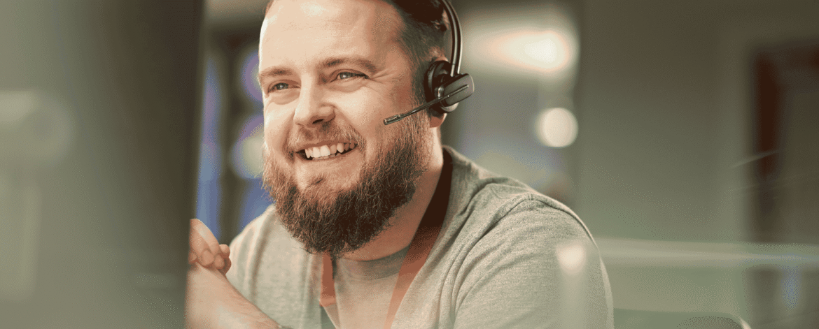 Smiling IT support specialist wearing a headset at a desktop monitor, the kind of help desk that walks agency staff through HIPAA encryption requirements for home health agencies.