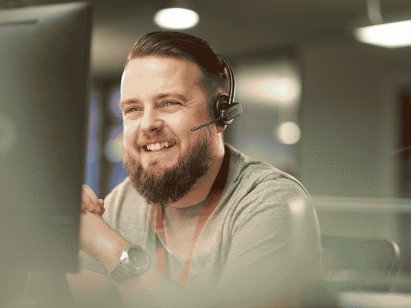 Image 1_8.31.26 Smiling IT support specialist wearing a headset at a desktop monitor, the kind of help desk that walks agency staff through HIPAA encryption requirements for home health agencies.