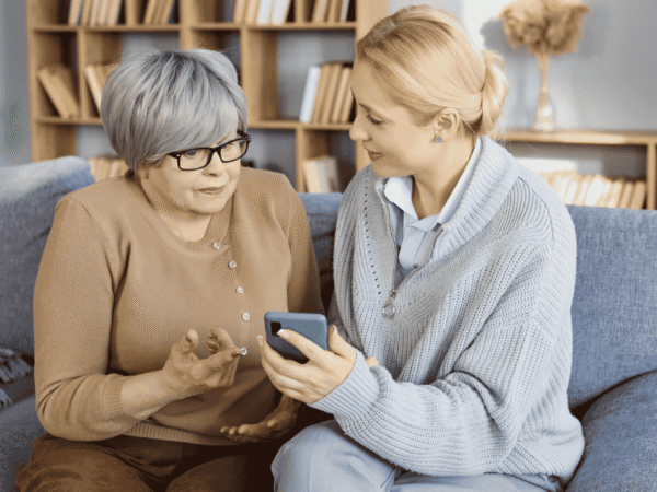 Image 1_9.7.26 Home health clinician and an older adult reviewing a smartphone at home, the patient data a HIPAA business associate agreement for home health agencies protects.