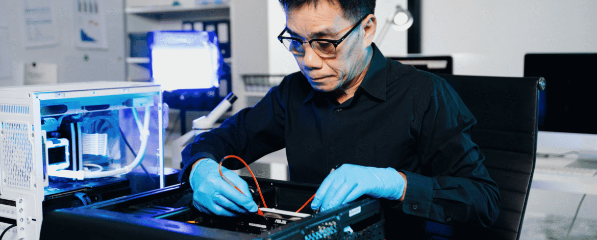 technician in blue gloves testing components inside an open desktop tower at a repair bench