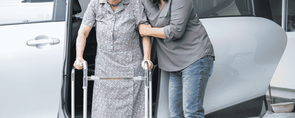 Caregiver steadying an older woman with a walker beside a van after a home visit, the care that precedes questions about HIPAA rules for deceased hospice patients.