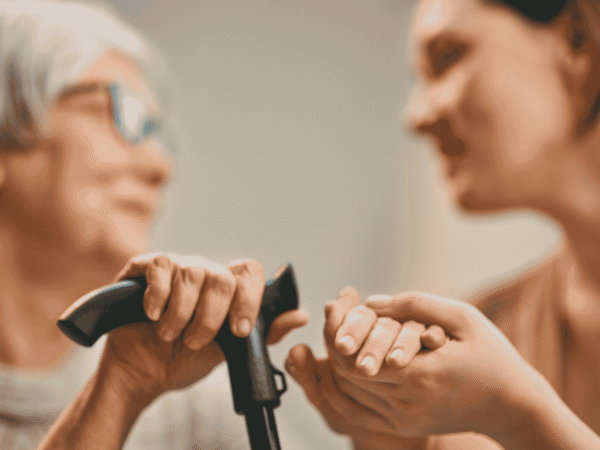 Image 1_9.14.26 Caregiver holding an older adult's hand beside a walking cane during a home visit, the patient relationship behind HIPAA breach notification for home health agencies.