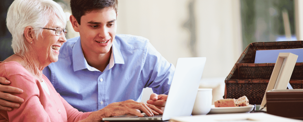 Older adult and a younger man reviewing a laptop together at her kitchen table, the setting behind decisions about outsourcing HIPAA compliance for home health agencies.