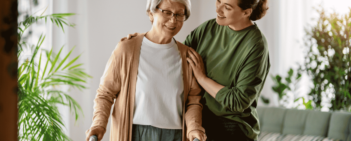 Older woman using a walker, steadied by an aide in a sunlit living room where the field devices in an ePHI asset inventory for home health agencies are actually used.