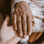 Nurse in blue scrubs settling a blanket around a seated senior client at home, the daily work behind the proposed HIPAA Security Rule for home health agencies.