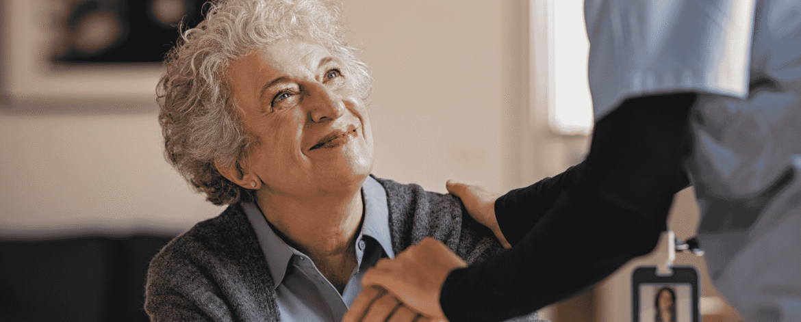 Caregiver wearing a photo identification badge resting a hand on a seated older woman holding a cane, the client records behind California's 30-day breach notification