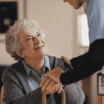Caregiver wearing a photo identification badge resting a hand on a seated older woman holding a cane, the client records behind California's 30-day breach notification
