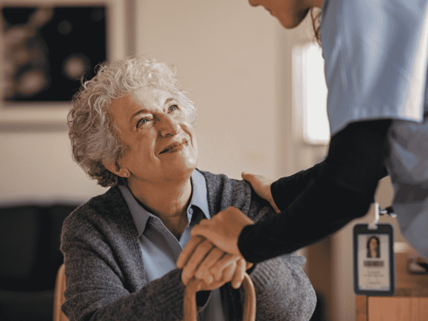 Caregiver wearing a photo identification badge resting a hand on a seated older woman holding a cane, the client records behind California's 30-day breach notification