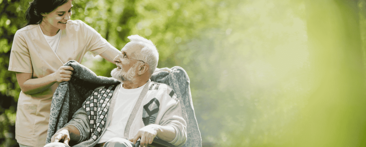 Caregiver wrapping a blanket around an older man in a wheelchair outdoors during a hospice visit, where ePHI travels on field devices subject to Security Rule safeguards.