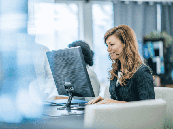 Image 3_9.4.26 Support agent in a headset typing at a desktop computer in a bright office, fielding questions such as whether public Wi-Fi is a HIPAA violation for home health clinicians.