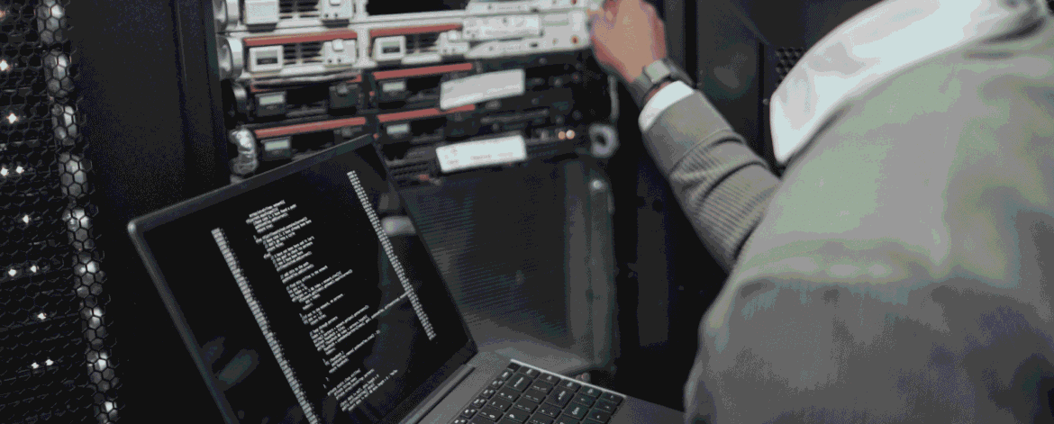 technician holding an open laptop while adjusting a server in a dark equipment rack