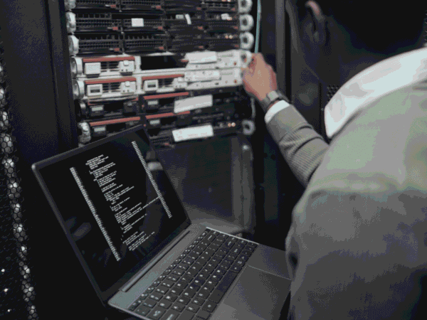 technician holding an open laptop while adjusting a server in a dark equipment rack