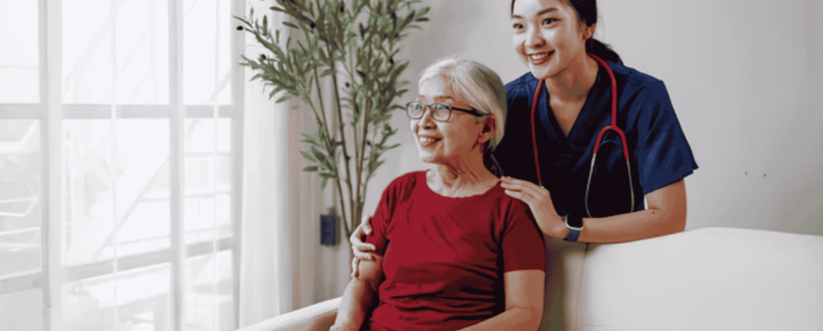 Nurse in navy scrubs beside an older client seated on a couch at home, the setting behind the question: is a stolen encrypted laptop a reportable HIPAA breach.