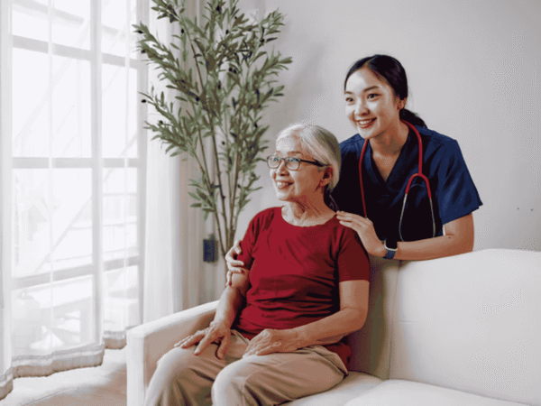 Nurse in navy scrubs beside an older client seated on a couch at home, the setting behind the question: is a stolen encrypted laptop a reportable HIPAA breach.